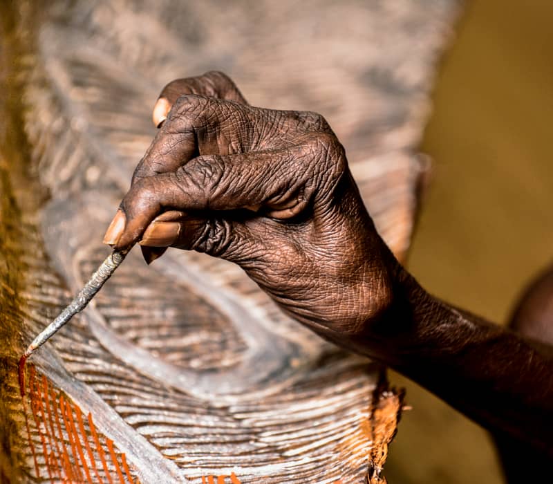 An artist at the Buku-Larrnggay Mulka Centre in Yirrkala, NT, applies traditional fine-line patterns to a bark painting.