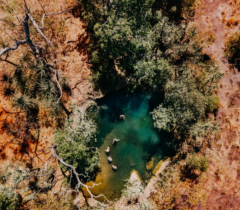 stunning top-down aerial shot of Marlee's Bath, a private, crystal-clear turquoise swimming hole tucked into the rugged sandstone landscape of Bullo River Station.