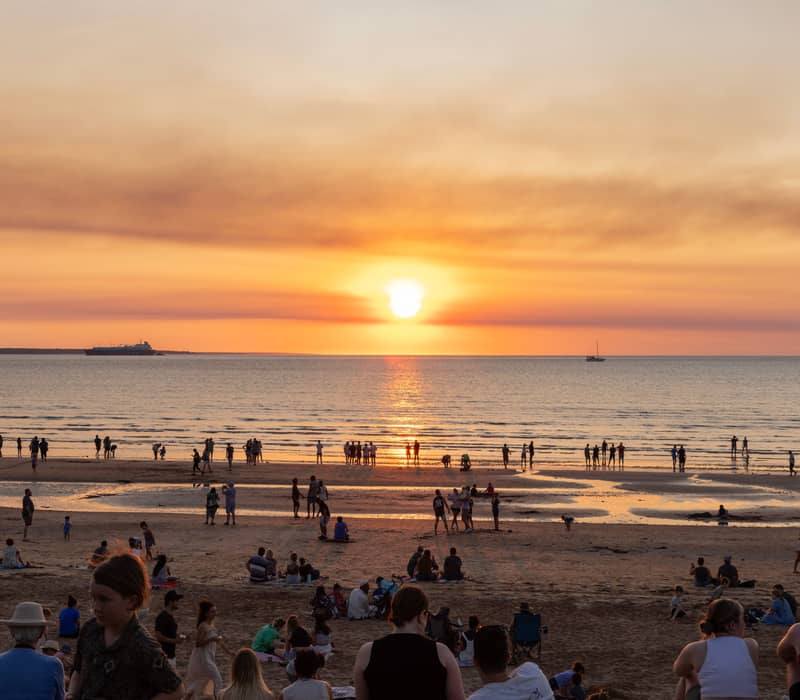 Crowds of locals and tourists sit on the sand at Mindil Beach to watch the sun dip below the horizon during the famous evening markets.