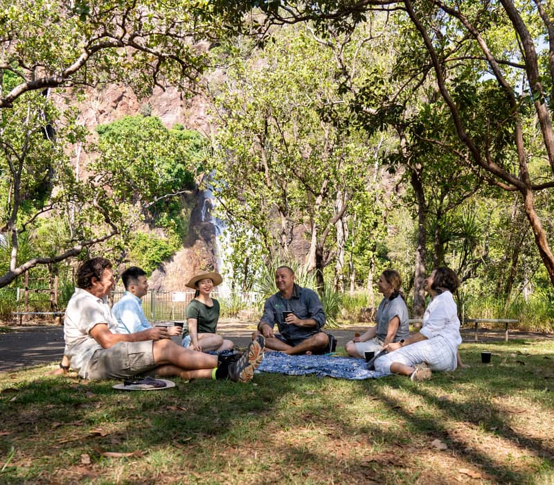 Guests on an Ethical Adventures tour enjoy a seated picnic lunch on a blue rug in the shade of a monsoon forest within Litchfield National Park.