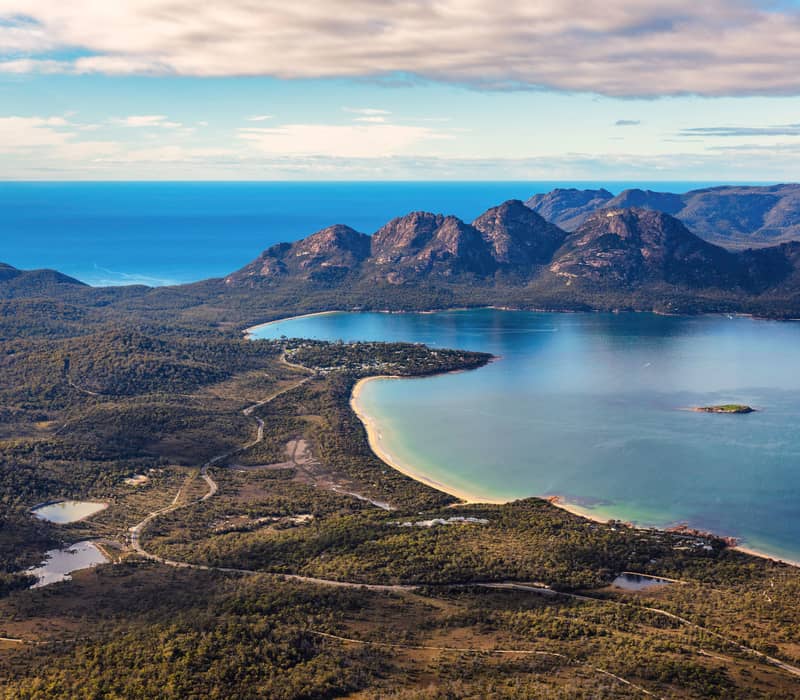 A spectacular high-angle aerial view capturing the settlement of Coles Bay nestled along the curve of the Freycinet Peninsula.