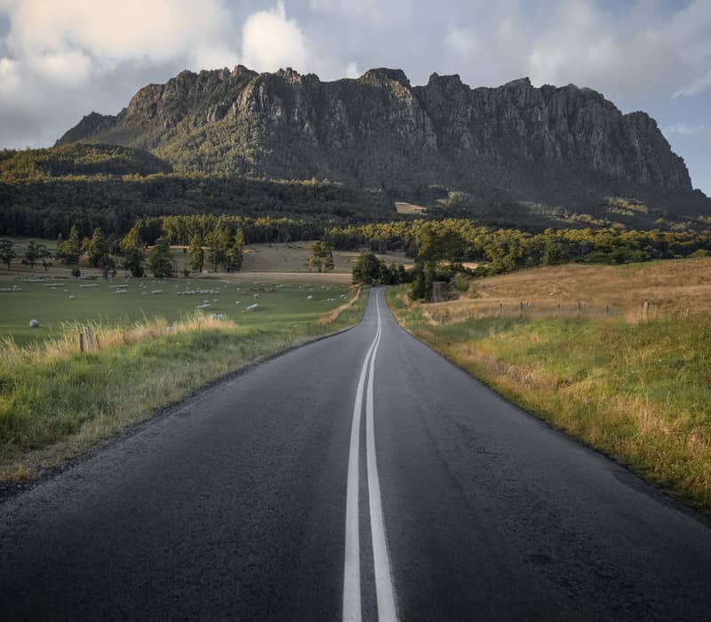 A long, straight road leads the eye toward the dramatic, jagged silhouette of Mount Roland near Sheffield.
