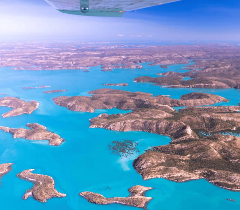Aerial view of rocky islands scattered in bright turquoise water under a clear sky.
