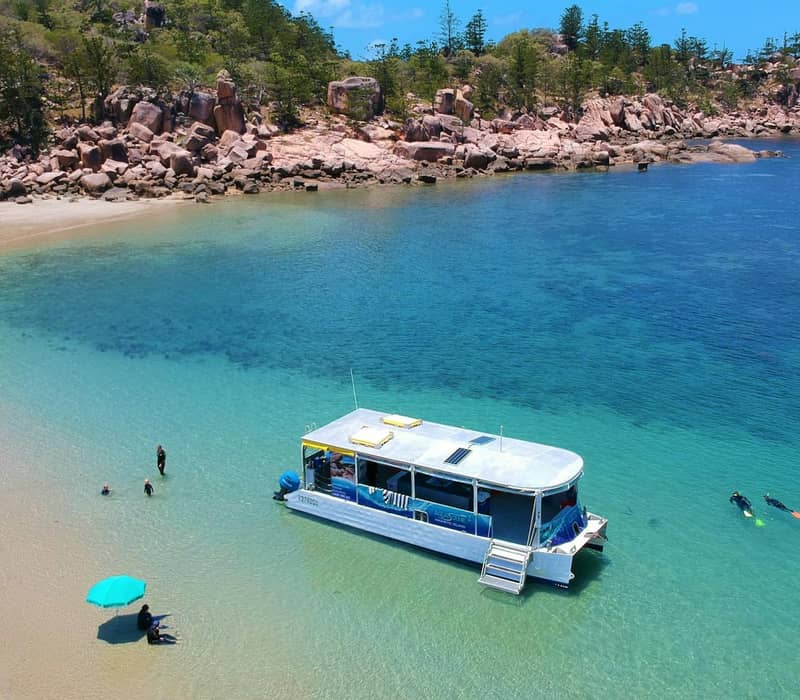 White snorkeling tour boat anchored near sandy beach and two snorkelers in clear blue water at Magnetic Island