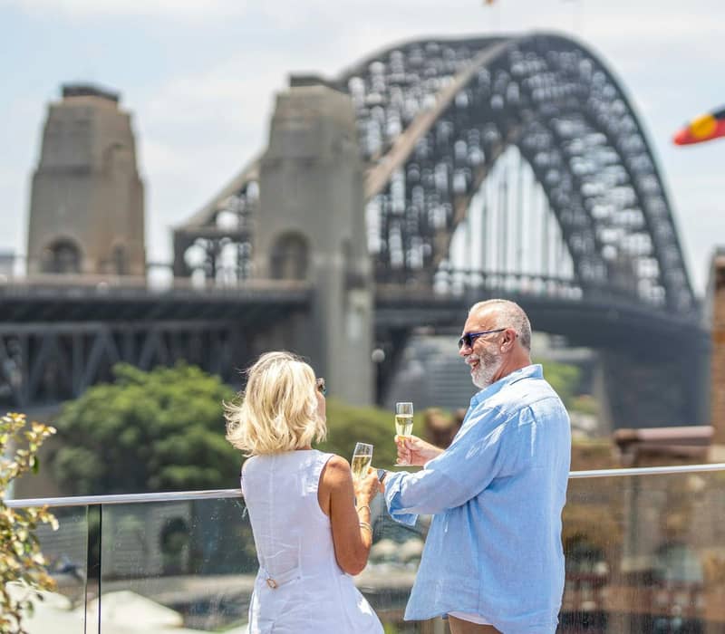 Couple toasting with champagne on balcony with Sydney Harbour Bridge in background
