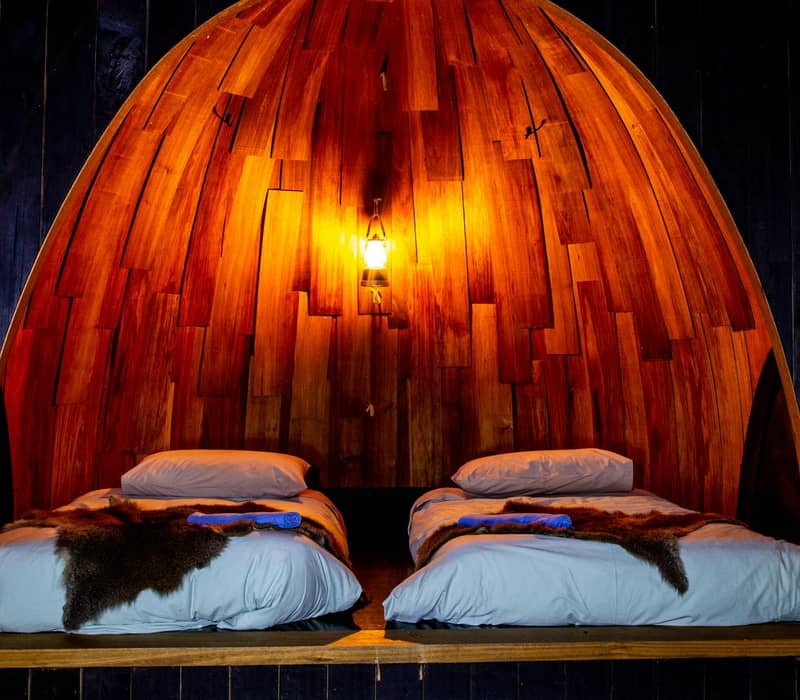 Two double beds inside a wooden cabin under warm light at night.